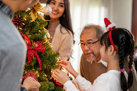 多代亚洲家庭装饰圣诞树爸妈女儿孩和祖父装饰圣诞树为快乐和节日的季问候做准备图片