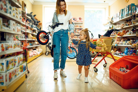 母亲和漂亮的小女孩在儿童商店购买自行车图片