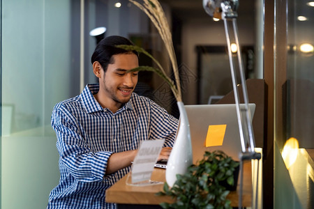 年轻的亚洲成人商坐在办公室的咖啡厅手持笔记本电脑到处都有智能办公室工作的概念背景图片