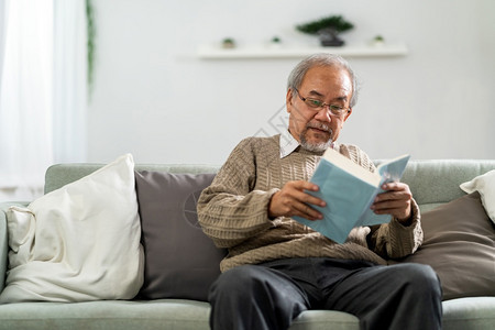 坐在客厅沙发上看小说的快乐亚洲退休老人图片