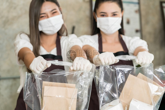 近身女服务员戴保护面罩带微笑拿着购物袋取走或外卖食品这项基本服务非常受欢迎而城市则被关闭无法使用科罗纳新冠19大流行病图片