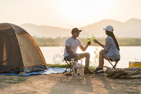 亚洲年轻成人夫妇在日落时帐篷露营区边喝啤酒图片