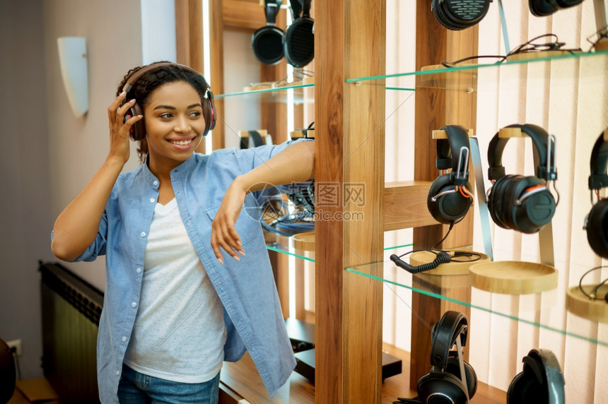 听耳机店音乐的年轻妇女音响店的青年带耳机在背景上展示的女青年多媒体沙龙的买家听音乐女青年耳机店图片