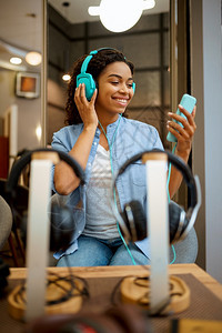 妇女听耳机店的音乐响女员工背景上用耳机展示的女员工多媒体沙龙的买家耳机店女员工听音乐图片