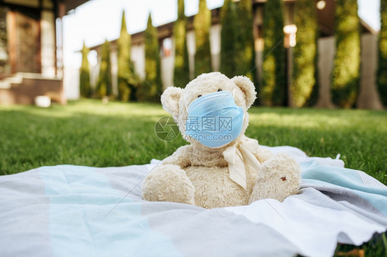 Teddy戴着保护的面具坐在花园的毯子上在后院的草坪上呼吸器装有软玩具流行病危险感染保健概念Teddy戴着保护面具坐在毯子上图片