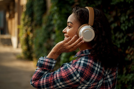 在夏季公园听音乐的女迷在户外行走女孩听耳机背景绿树图片