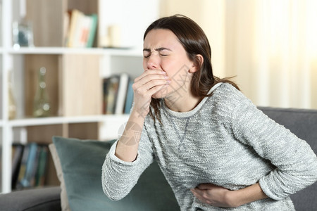 肚子痛的紧张女人准备在家里沙发上呕吐图片