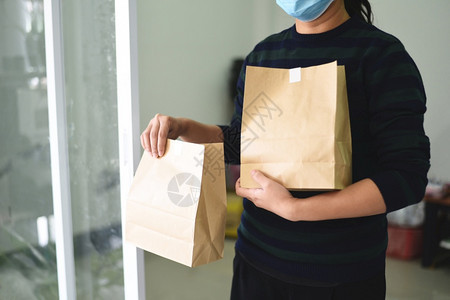 佩戴保护面罩冠状和手持架的分娩妇女用纸食品包装袋服务邮递员快送外食品回家服务图片