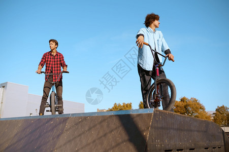 Bmx骑自行车者站在斜坡上滑板场接受培训极端自行车运动危险循环街头骑车青少年在夏季公园骑自行车Bmx骑自行车者站在斜坡上滑板场接图片
