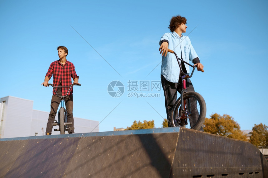 Bmx骑自行车者站在斜坡上滑板场接受培训极端自行车运动危险循环街头骑车青少年在夏季公园骑自行车Bmx骑自行车者站在斜坡上滑板场接图片