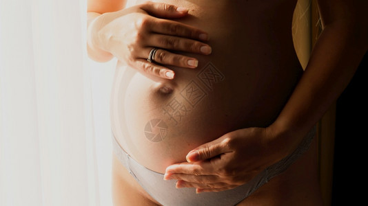 窗户旁边的孕妇抚摸肚子图片