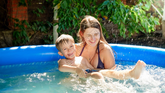 快乐的妈抱着微笑母亲支持她儿子在充气游泳池家庭暑假和节日图片