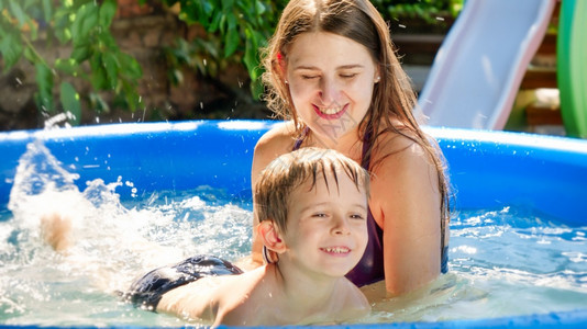 快乐的妈在家庭后院花园的游泳池里教她儿子游泳家庭暑假和期图片