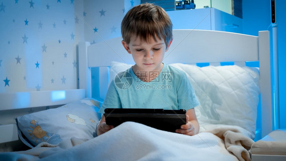 晚上坐在床看平板电脑录像的小男孩肖晚上有小男孩的肖像晚上有小男孩的肖像晚上在平板电脑看录像图片
