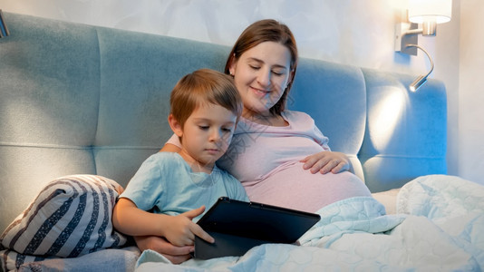 小男孩和孕妇晚上在床上使用平板电脑图片