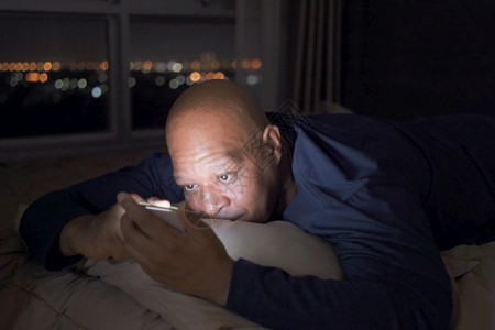 抑郁的黑人老非裔美国在社交媒体互联网上使用智能手机睡在家中卧室的床上深夜在技术设备概念方面的生活式因失眠图片