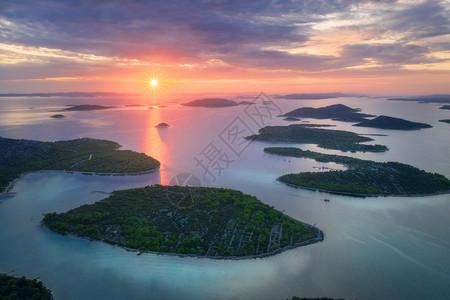 克罗地亚夏季日落时得里海美丽的小岛空中景象蓝水山上的绿树多彩天空云和橙色的太阳图片