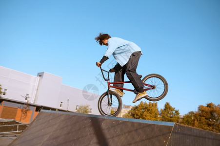 Bmx骑自行车者在斜坡上耍花招在滑板场上玩耍的青少年参加滑板场训练的青少年极端自行车运动危险的自行车运动危险的街头骑车在夏季公园图片