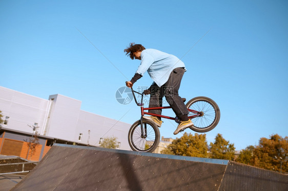 Bmx骑自行车者在斜坡上耍花招在滑板场上玩耍的青少年参加滑板场训练的青少年极端自行车运动危险的自行车运动危险的街头骑车在夏季公园图片