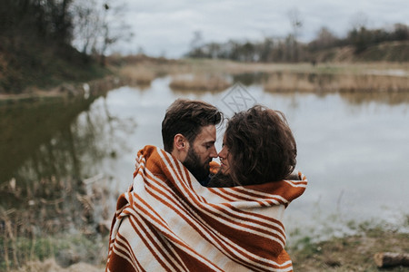 两对天主教情人在湖边裹着毯子年轻夫妇在秋天户外拥抱一个有胡子的男人和卷毛女在爱中情节爱与家庭的概念两个有胡子的情人在湖边裹着毯子图片