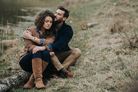 快乐的情侣坐在湖岸边拥抱图片