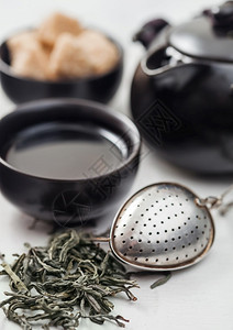 新鲜的有机松开绿茶在白桌背景上配有教练喷雾器黑茶壶和甘蔗糖图片