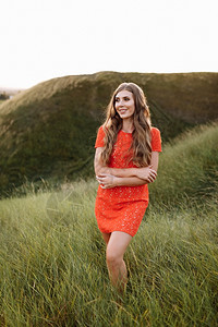 在田野的绿草地上穿着红色礼服的漂亮女人肖像在暑假自然在日落的时候公园里长卷发的女孩在田野上的绿草地穿着红色礼服的漂亮女人肖像在公图片