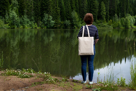 站在湖边的妇女携带空可再用购物袋模型女手拿着帆布生态友好型袋模拟图片