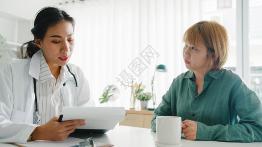 使用剪贴板穿白制服的亚洲年轻女医生正在发表精彩的新闻谈话讨论结果或症状让女病人坐在诊所或医院办公室的书桌旁图片