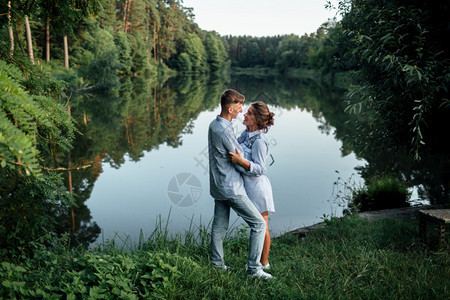 年轻夫妇在阳光明媚的日子里拥抱和在湖边走动男女在暑假时都湖边走动可爱家庭的概念有选择焦点年轻夫妇在阳光明媚的日子里拥抱和在湖边走图片