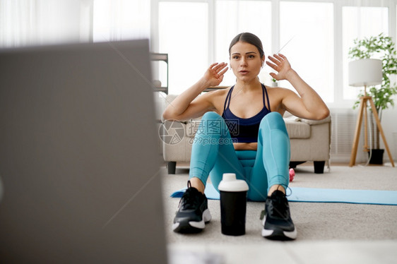 Slim妇女坐在垫子上线健身培训笔记本电脑上女运动员穿服网上锻炼背景室内女坐在垫子上线健身培训图片