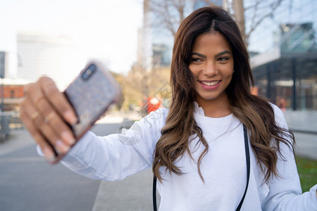 年轻女在户外站立时用摩菲手机自拍的肖像城市概念图片