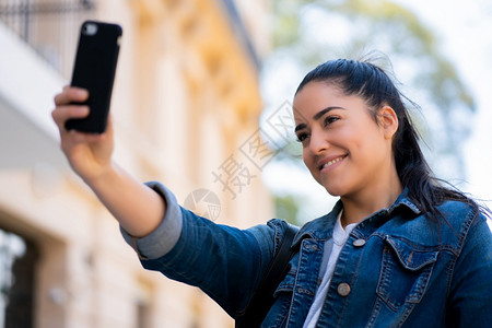 年轻女在户外站立时用摩菲手机自拍的肖像城市概念图片