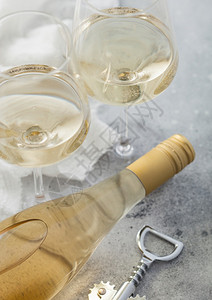 两杯水晶和一瓶白自制葡萄酒在光桌背景上配有钢软木塞图片