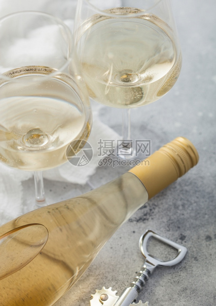 两杯水晶和一瓶白自制葡萄酒在光桌背景上配有钢软木塞图片