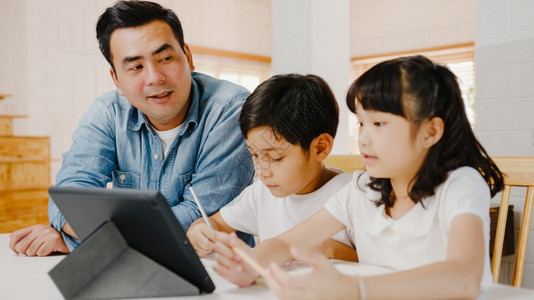 父亲教孩子们在家里的客厅使用数字平板电脑在一起的时间自我隔离社交不和为预防冠状而隔离图片