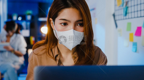 快乐的亚洲女商人戴着医疗面罩在新的正常情况下在预防的正常情况下用笔记本电脑在办公室晚上班科罗纳后的生活和工作图片