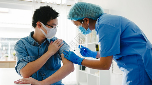 向老年男患者提供新冠19或流感抗疫苗的亚洲年轻女护士在保健诊所或医院办公室戴面罩防止疾图片