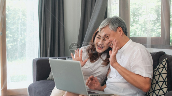亚裔老人夫妇在家的视频电话亚洲裔老年人祖父母使用笔记本电脑视频话与家庭孙子女儿童交谈同时躺在家里客厅的沙发上图片