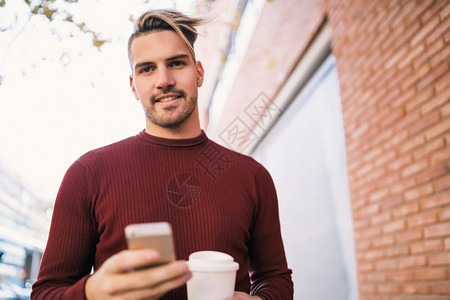 年轻英俊男子在街上露天喝咖啡时使用手机的肖像图片