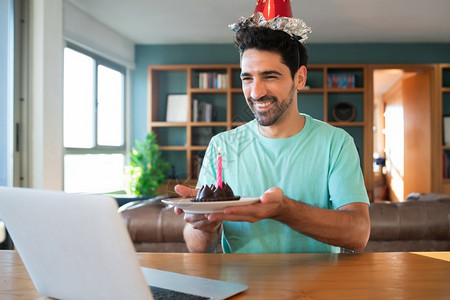年轻人在家中用笔记本电脑和蛋糕打来的视频电话上庆祝生日的肖像图片