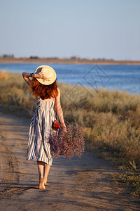 一个戴着帽子的女孩带着一束花沿海岸走来去图片
