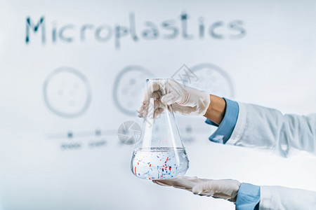 微塑料污染概念科学家持有一个装满微小塑料粒水样的瓶子与带有微塑料污染图的白板对着一个装有微塑料小粒的水样板图片
