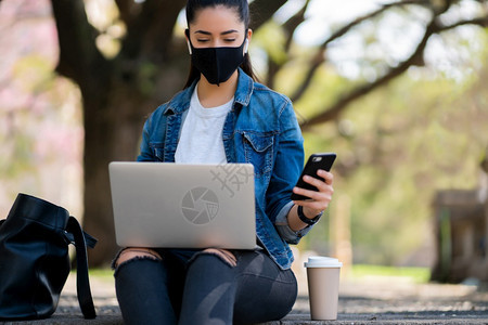 青年妇女在户外活动时使用手机和笔记本电脑的肖像城市概念新的正常生活方式概念图片