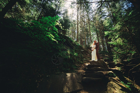 新婚娘在夏日的绿林中快乐新婚娘穿着长白色礼服新郎穿着红色西装新郎在婚礼当天拥抱新婚夫妇在夏天的绿林中快乐新婚娘穿着长白色礼服新郎图片