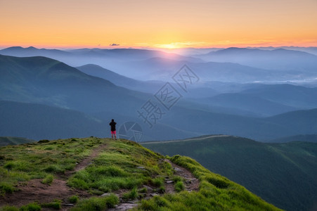 山顶上的运动男子在山峰上仰望着谷在欧洲夏季的多彩日落时阳光照耀着太有旅行者迷雾山森林陷落令人惊叹的天空和阳光风景图片