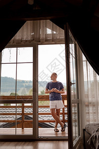 青年男子上午站在旅馆阳台上手里拿着咖啡或茶杯望着自然林和山外青年男子上午站在旅馆阳台上手里拿着咖啡或茶杯图片