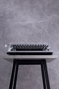 在靠近灰墙背景表面壁底表面的凳或架子上编剧复写概念的旧式打字机图片