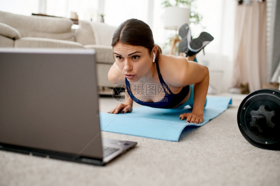微笑的女孩坐在地板上笔记本电脑上进行在线健身培训参加运动服互联网锻炼室内房间的女微笑孩坐在地板上线健身培训图片