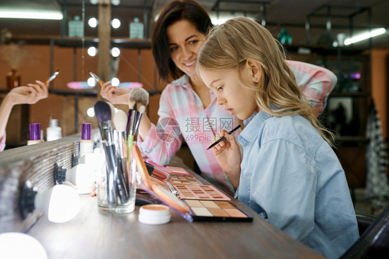 母亲和女儿在化妆沙龙使用影子调色盘妈和小女孩一起玩发型师快乐的童年迷人家庭母亲和女儿一起用影子调色盘化妆图片